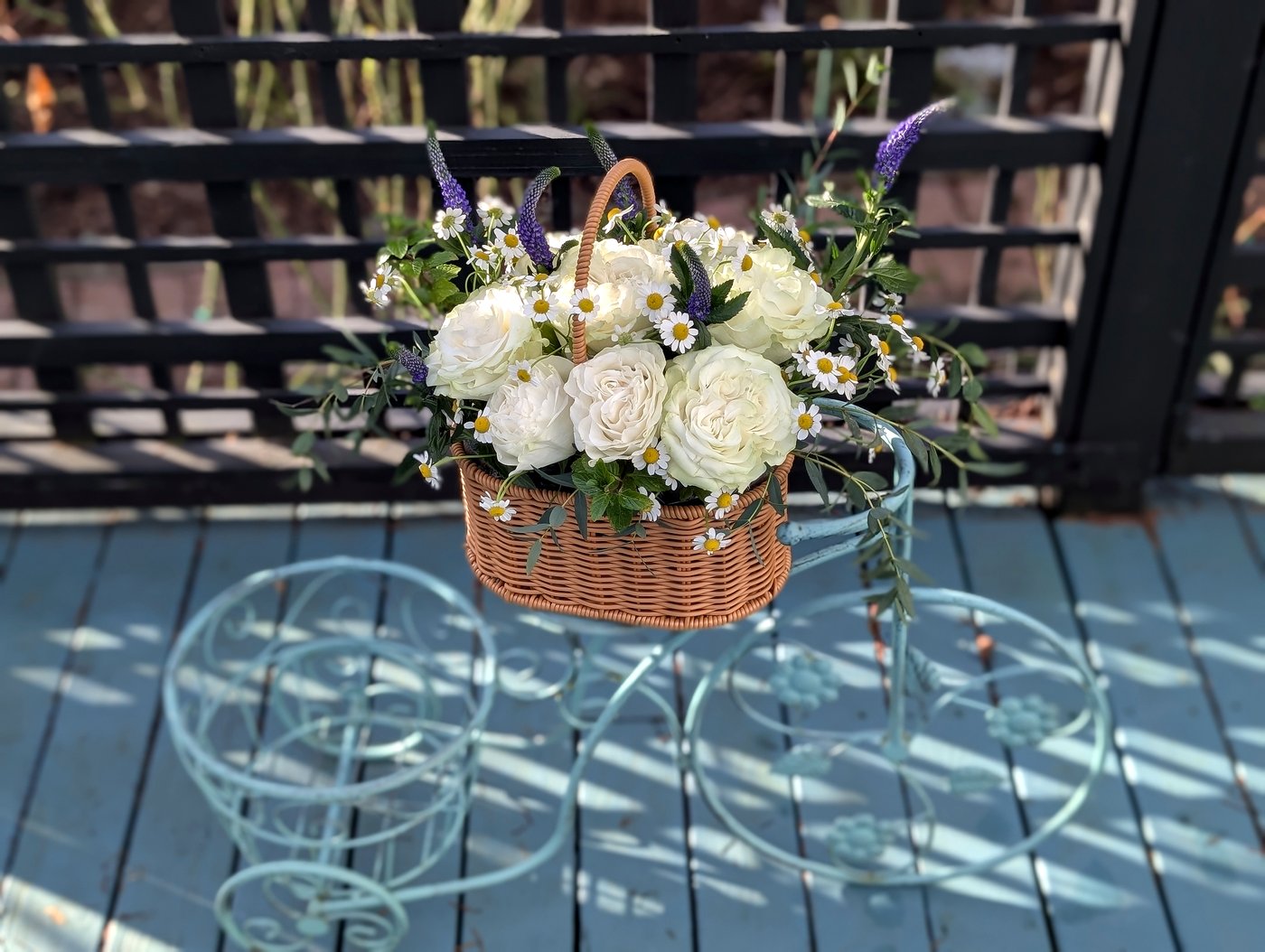 Basket of white garden roses, chamomile, and lavender resting on a vintage bicycle plant stand