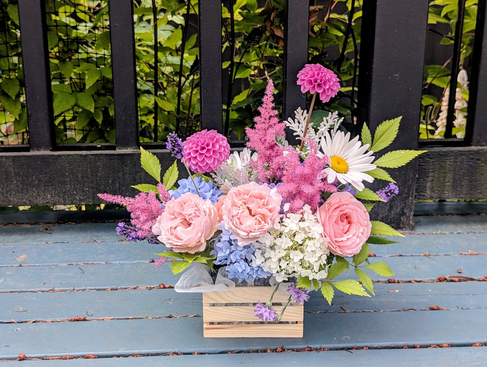 Summer arrangement in a wooden crate with pink garden roses, pompon dahlias, astilbe, blue and white hydrangea, and a Shasta daisy