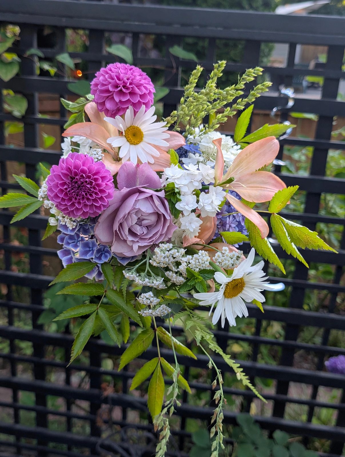 Midsummer hand-tied bouquet with magenta pompon dahlias, a lavender garden rose, peach lilies, white daisies, phlox, and yarrow